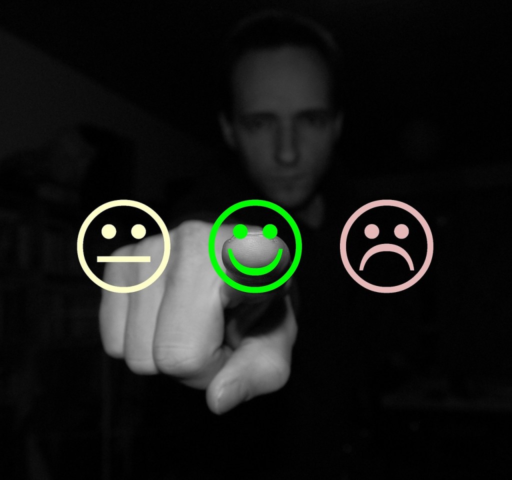 A selection of faces indicating satisfaction levels. From behind a man is indicating the most positive